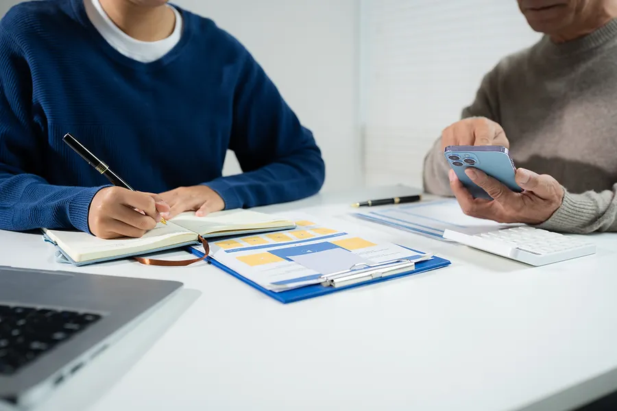 Anotando el presupuesto familiar en una libreta junto a una calculadora y un portátil