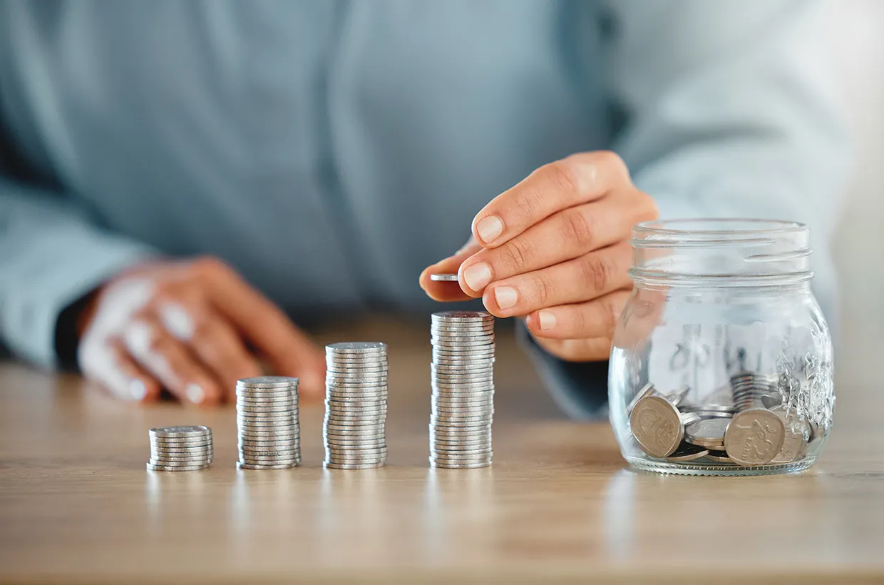 Monedas apiladas y un bote de ahorro sobre una mesa, símbolo de la planificación financiera personal